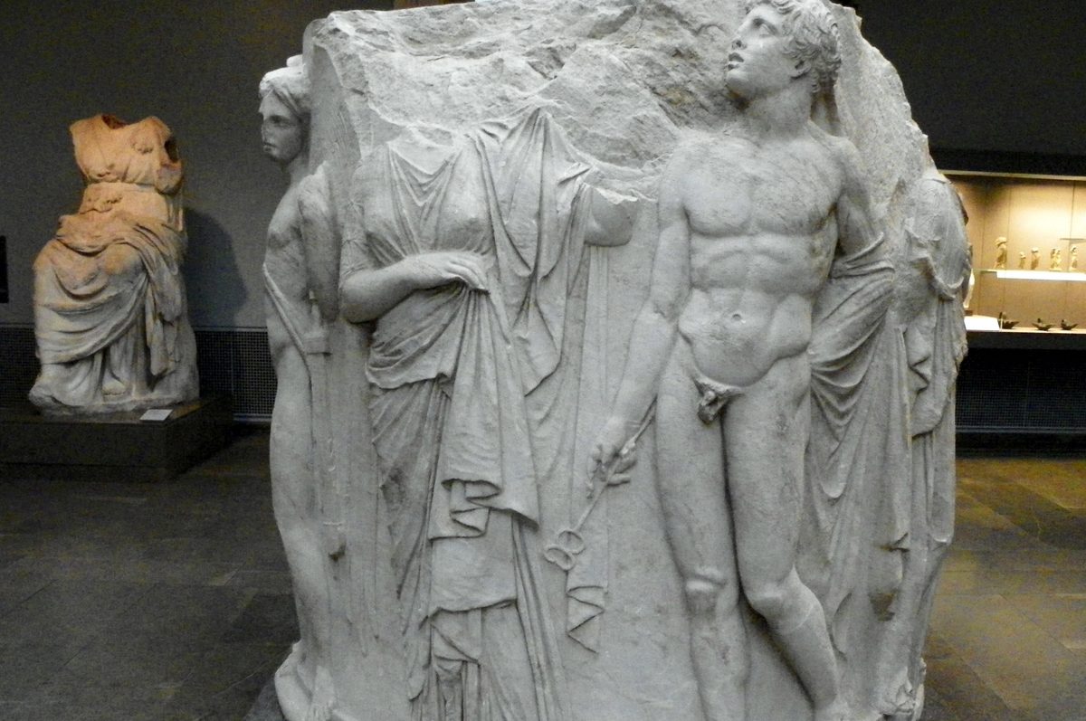 A carved marble column drum from the Temple of Artemis at Ephesus in the British Museum, with the god Hermes holding a staff beside a robed woman and a winged figure in high relief