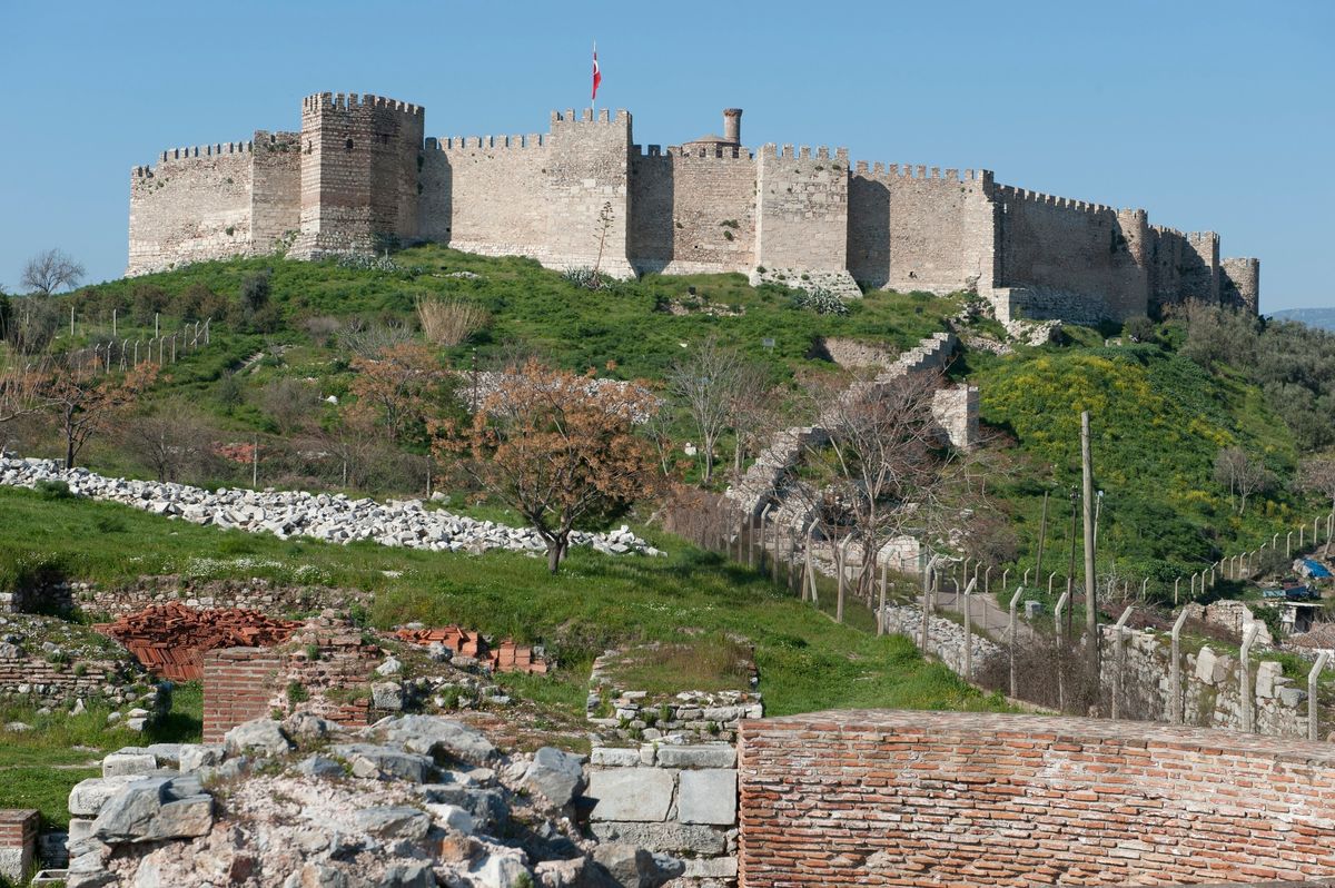 The crenelated walls and towers of Ayasuluk Fortress on its green hilltop in Selçuk, seen above the brick ruins of the Basilica of St John