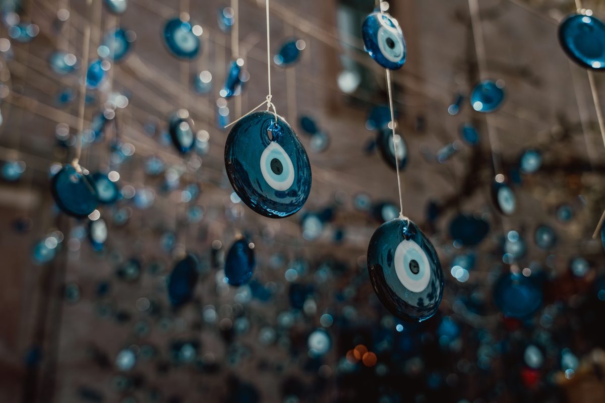 Blue glass evil-eye beads hanging on white threads in front of a softly blurred curtain of more beads