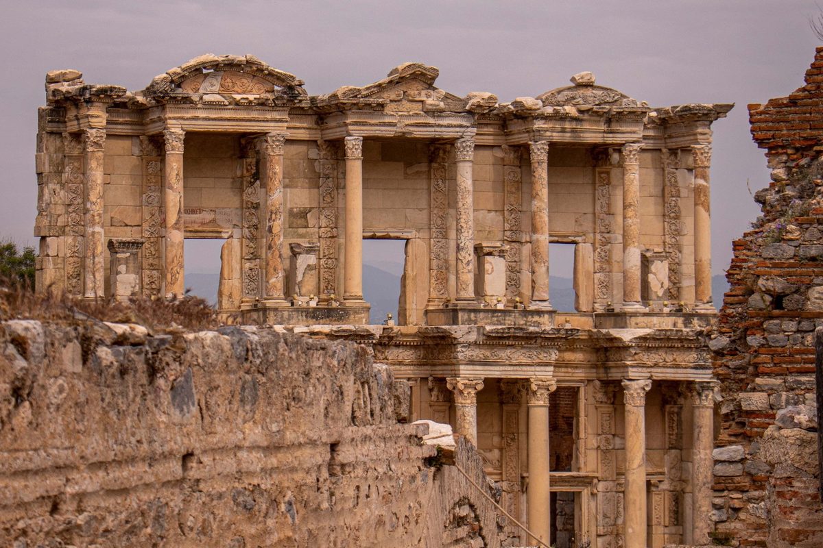 The two-story façade of the Library of Celsus seen over a ruined wall, with open sky and distant hills showing through its upper windows