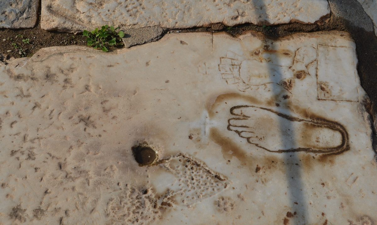 Ancient graffiti carved into a marble paving slab at Ephesus, showing a footprint and a female figure