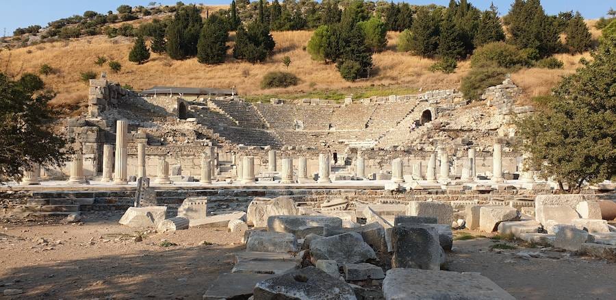 The semicircular stone seating of the Odeon at Ephesus with its columns and stage wall below a pine-covered hillside