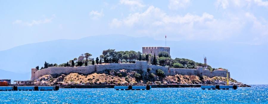 Pigeon Island in Kuşadası with its stone fortress walls, tower and flag seen across the blue Aegean