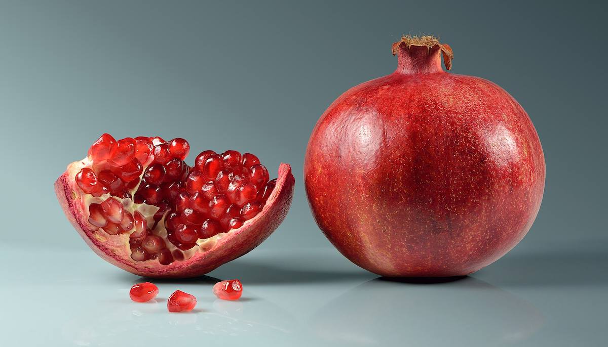 A whole red pomegranate beside an open half full of glossy red seeds