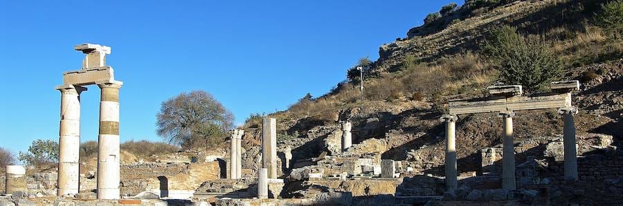 Re-erected columns and architraves of the Prytaneion at Ephesus below a dry hillside under a deep blue sky