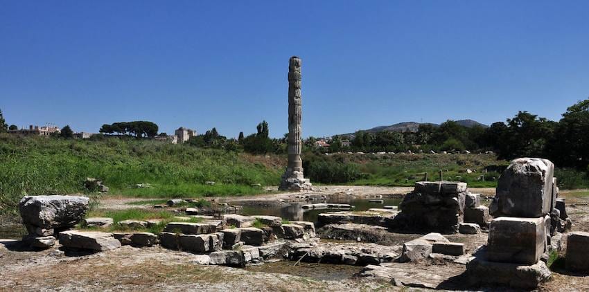 A single reconstructed column standing among the flooded stone foundations of the Temple of Artemis