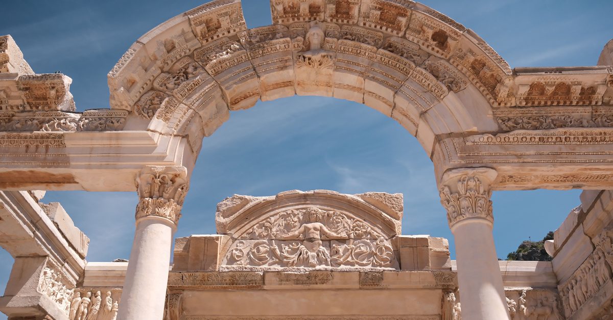 Carved arch of the Temple of Hadrian in Ephesus with a female bust on the keystone and a relief figure among scrolls behind it