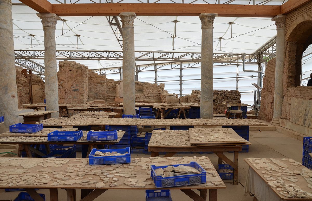 Tables covered with thousands of marble fragments under the protective roof of the Terrace Houses at Ephesus, between Roman columns and ruined walls