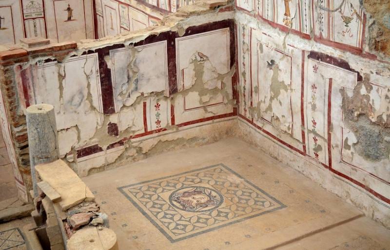 Painted Roman wall panels above a geometric mosaic floor with a central medallion in the Terrace Houses of Ephesus