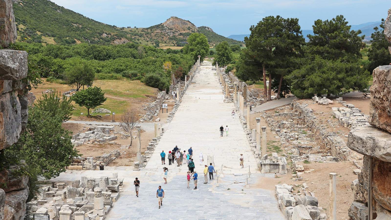 Harbor Street in Ephesus seen from the top of the Great Theater, its marble paving running straight between broken columns to a line of trees where the harbor once was